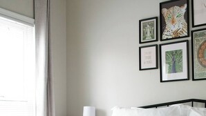 Un lit bien fait, avec du linge de lit blanc, une tête de lit en métal noir et une table de chevet sur laquelle se trouvent une lampe et une plante.