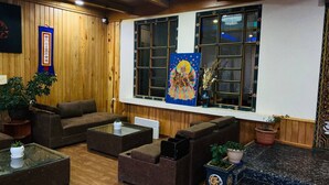 A cozy room with wooden paneling, a large window with a colorful painting, and several sofas and tables. - Tsherim Resort (Paro)