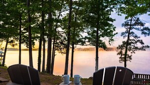 A lakeside deck with Adirondack chairs and a table, overlooking a calm lake and forested area.