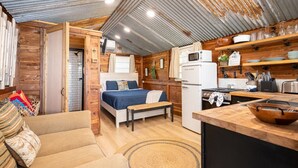 A compact, rustic cabin-style room with a bed, kitchenette, and a small seating area.