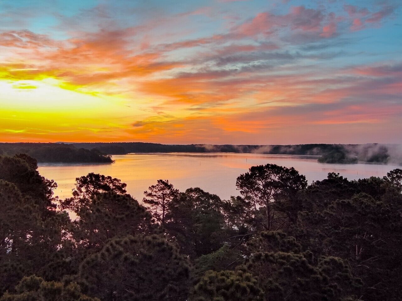 A sunset over a lake with trees in the foreground.