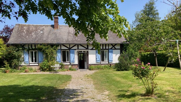 Une maison traditionnelle à colombages, avec un chemin de gravier menant à l’entrée, entourée d’un jardin bien entretenu et d’arbres.
