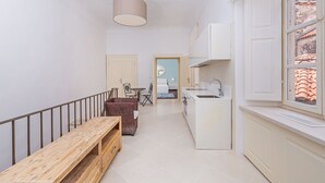Un couloir étroit avec un banc en bois, un coin repas avec une table et des chaises, et une cuisine équipée d’un évier et de placards.