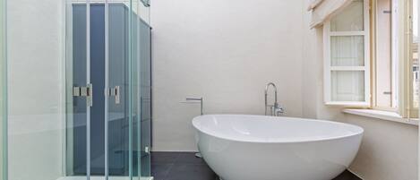 Un baño moderno con una bañera independiente, una cabina de ducha con paredes de cristal y un ventanal con marco blanco.