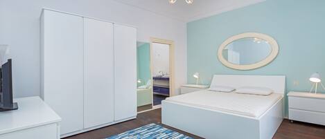 Un dormitorio moderno con una cama grande, un armario, un espejo y un televisor sobre un soporte.
