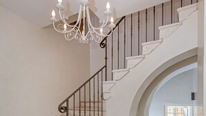 Un escalier aux marches blanches et aux balustrades noires, menant à un palier où se trouvent une petite table blanche et un lustre.