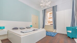 Une chambre moderne avec un grand lit, une armoire, un fauteuil bleu et une vue sur la ville par la fenêtre.