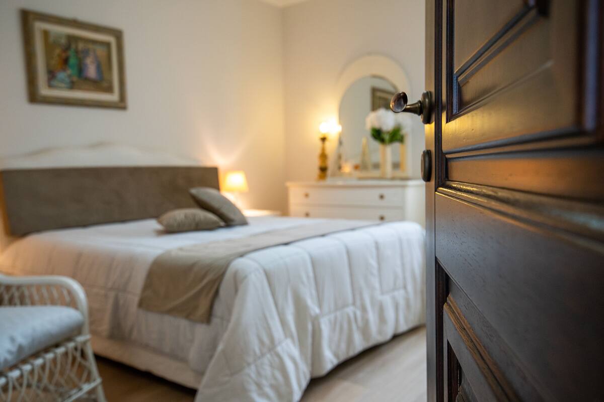 A bedroom with a bed, bedside table, lamp, and a mirror on the wall.