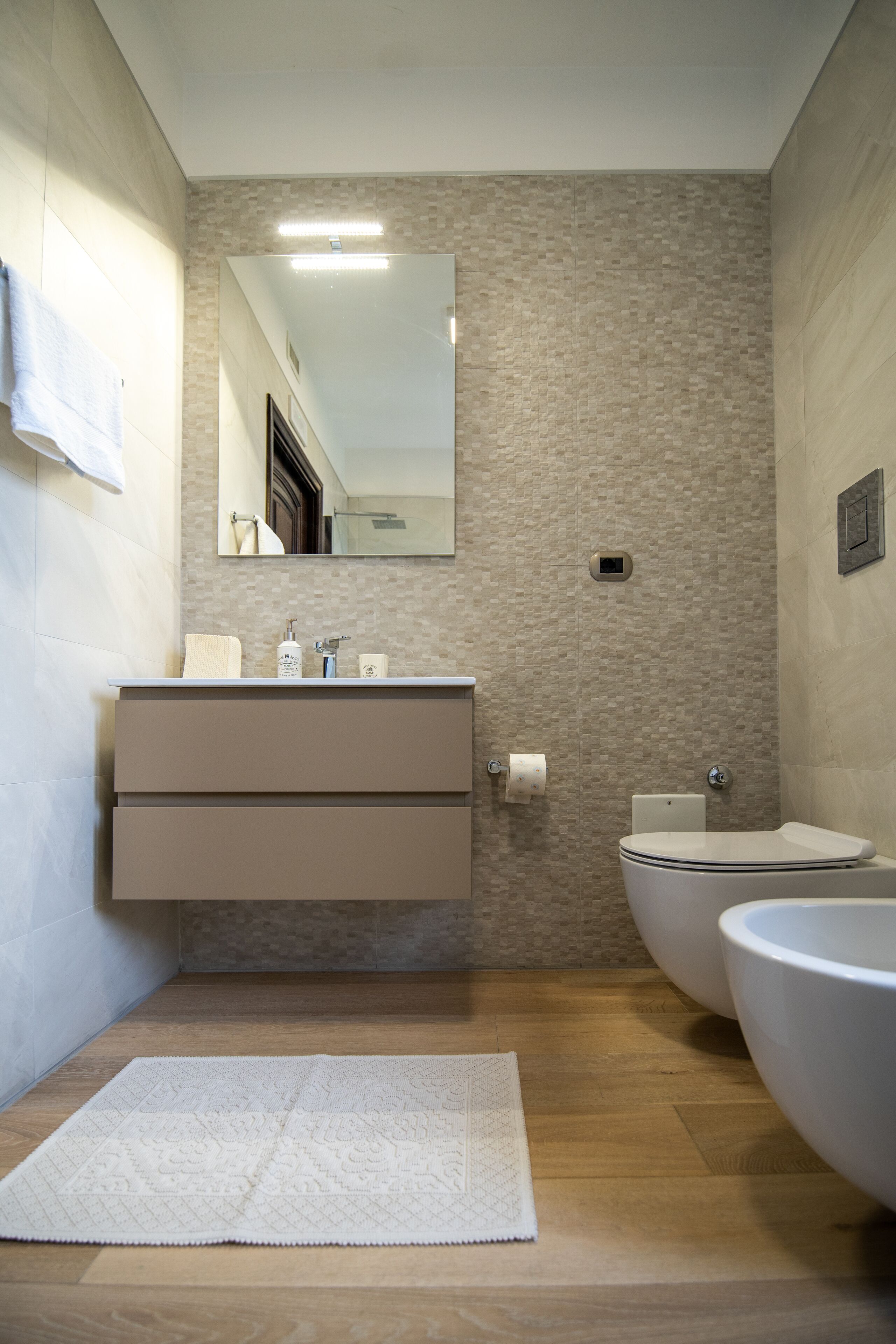 Un bagno moderno con pavimento in legno, un lavandino bianco, uno specchio grande e un water.