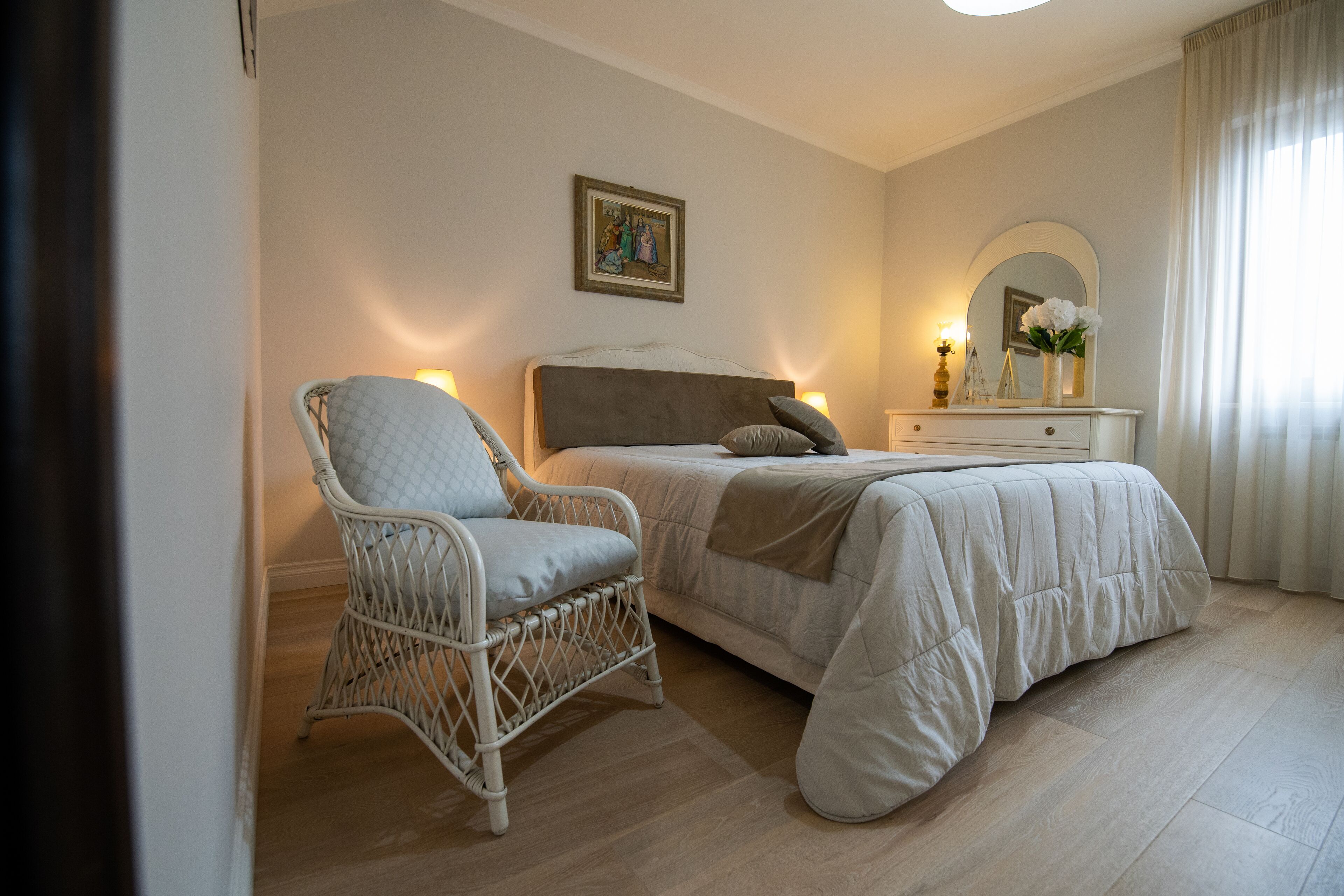 A bedroom with a bed, a wicker chair, a dresser, and a mirror.