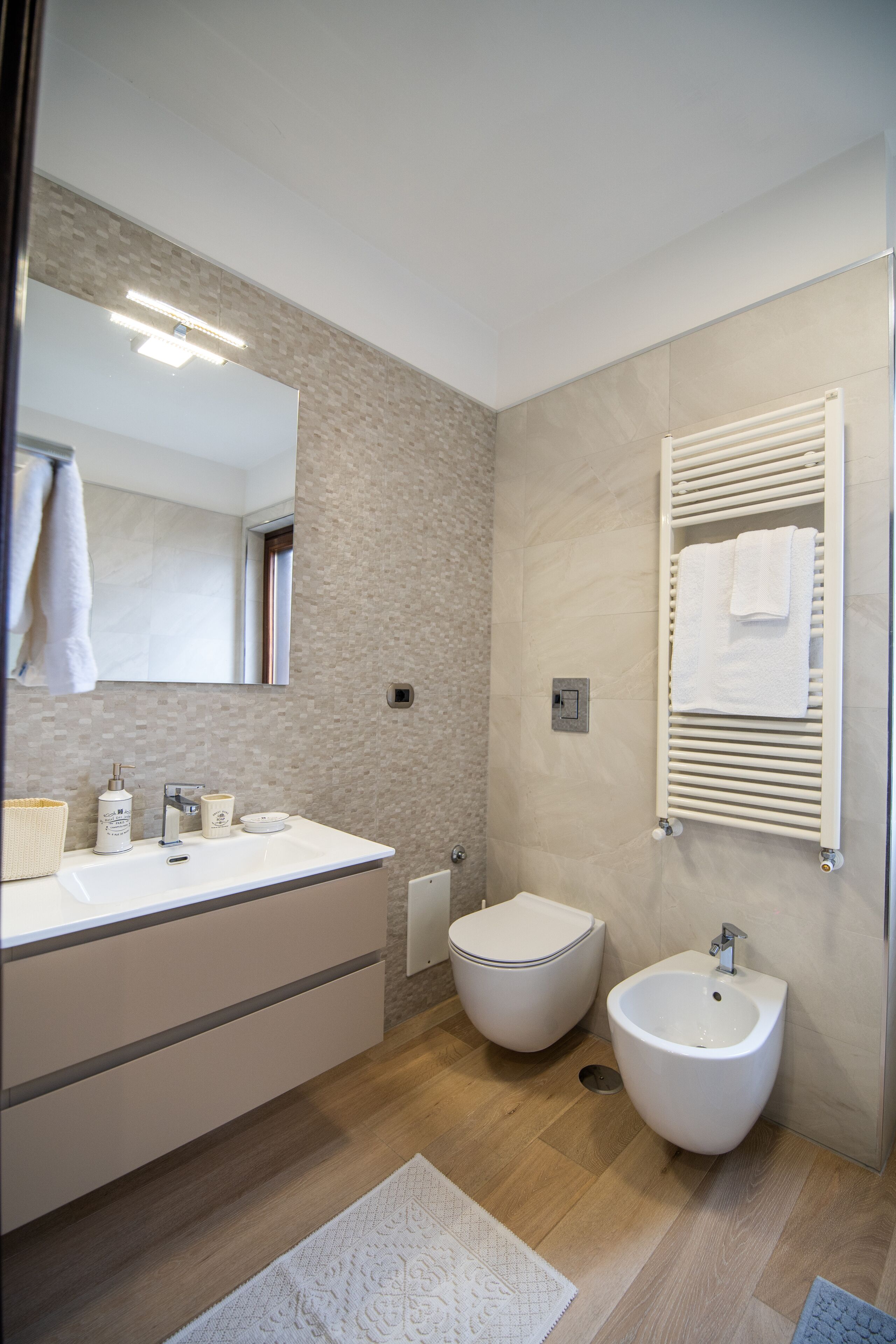 A modern bathroom with a large mirror, a sink, a bidet, and a towel rack.