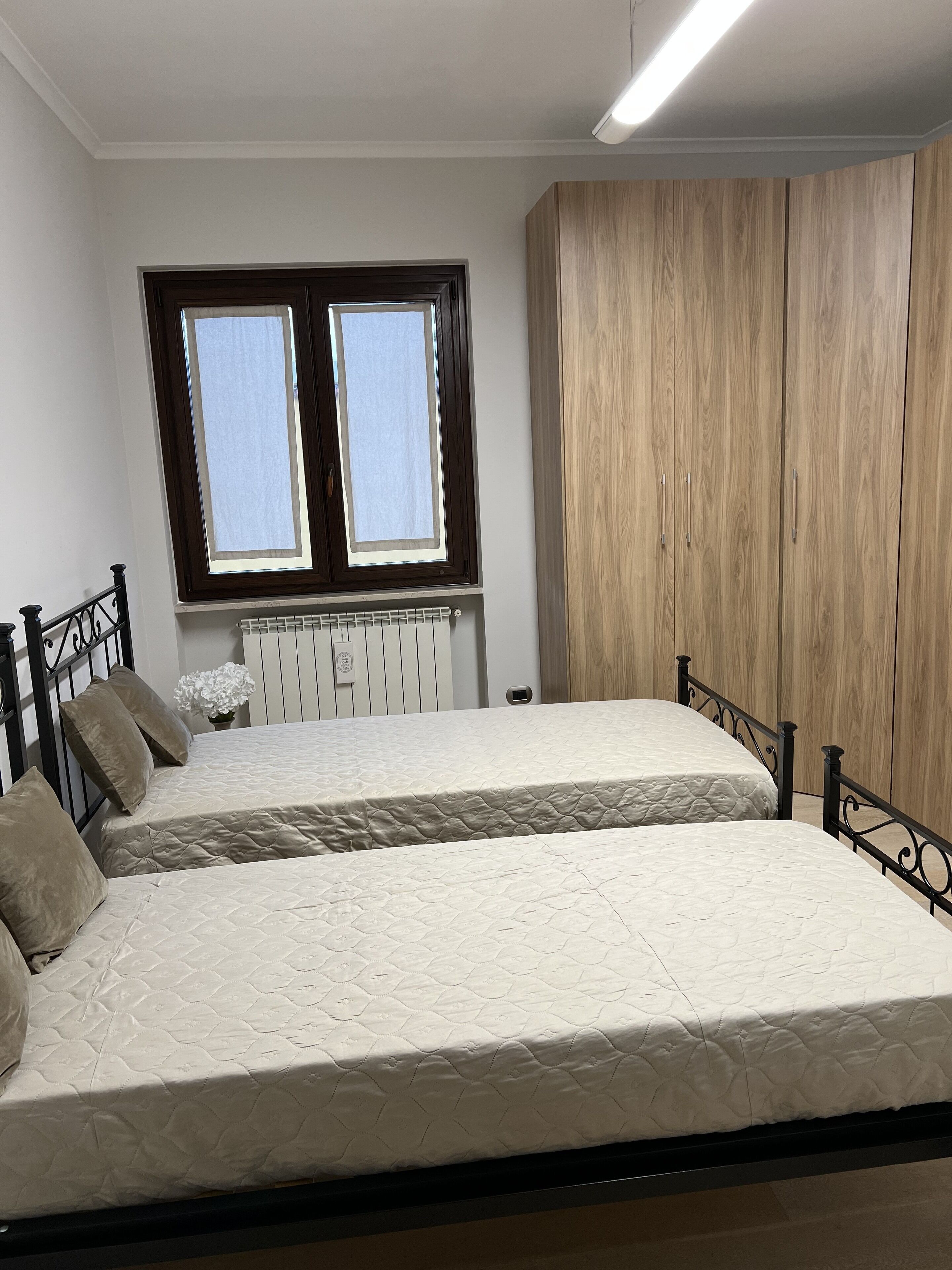 Une chambre avec deux lits, une fenêtre, un radiateur et une armoire.