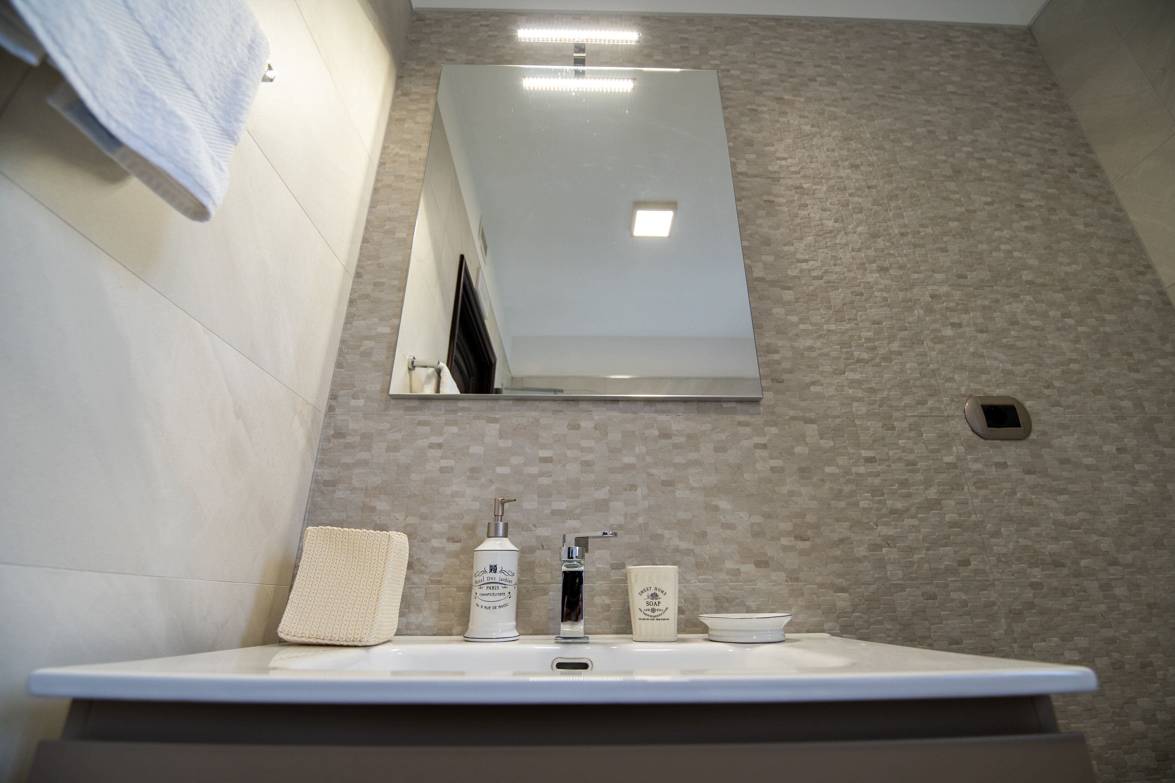 Een badkamer met een wit wastafelmeubel, een spiegel erboven en een handdoek aan de muur.