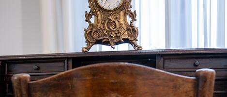 A wooden chair with a cushioned seat and a desk with a decorative clock.