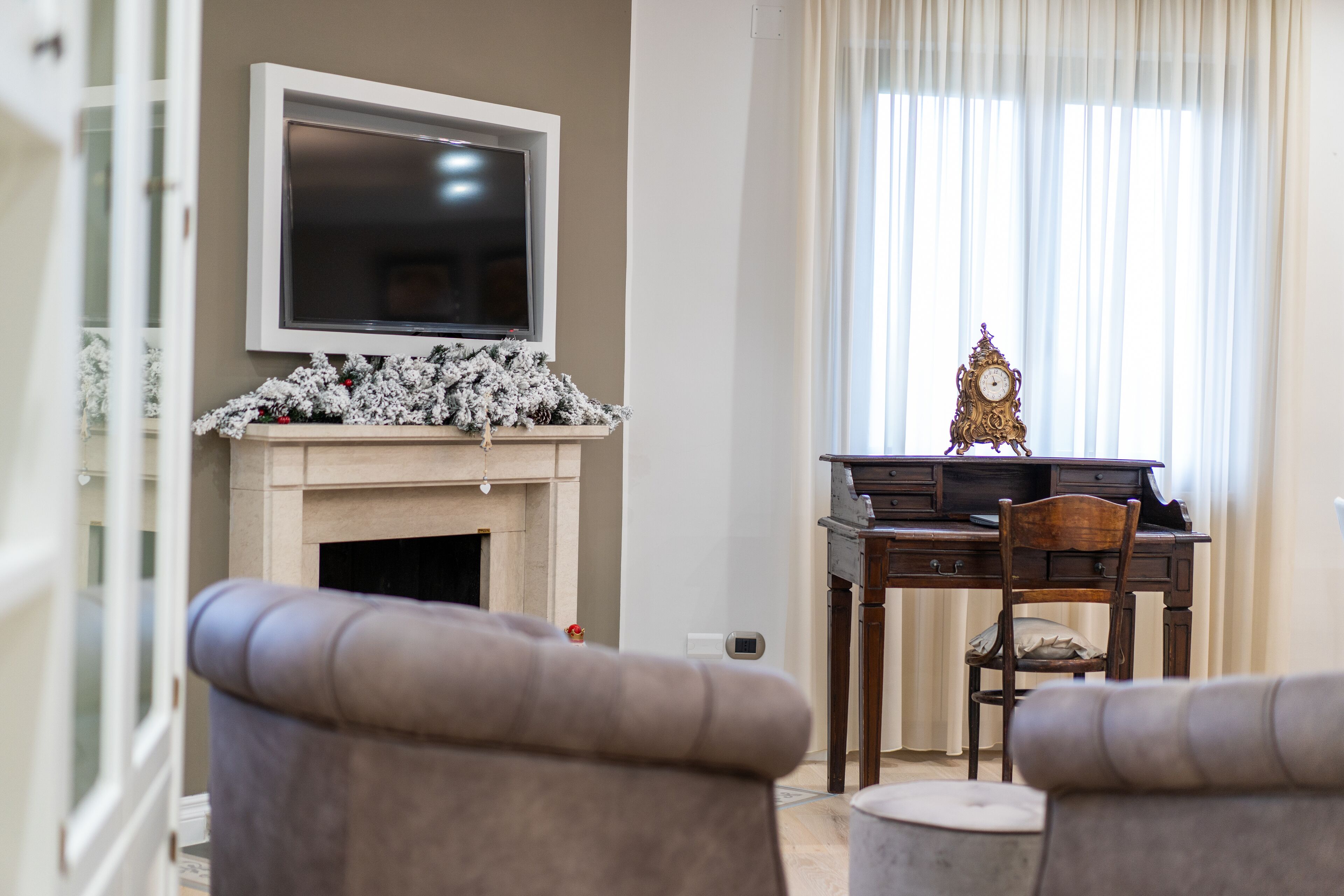 Un salon avec une cheminée, un téléviseur fixé au-dessus, un bureau en bois avec une chaise et deux fauteuils.