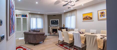 Una sala de estar moderna con chimenea, un comedor con sillas blancas y una alfombra roja estampada.