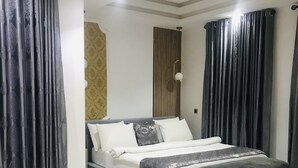 A modern bedroom with a large bed, grey curtains, and a light fixture on the ceiling. - De Fivez Hotel (Lekki)