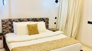 A hotel room with a large bed, a patterned headboard, a bedside table, and a wall-mounted air conditioning unit. - De Fivez Hotel (Lekki)