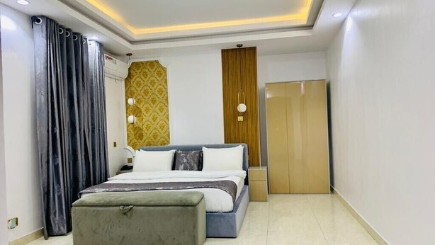 A modern bedroom with a bed, bedside table, and a wardrobe. - De Fivez Hotel (Lekki)