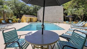 A pool area with lounge chairs and a table under a large umbrella.