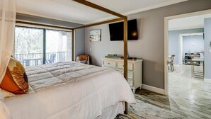 A bedroom with a four-poster bed, a large window, a flat-screen TV, and a view of the outdoors.