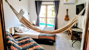 Une chambre avec un lit-hamac, deux lits simples, une guitare, une télévision et une vue sur une piscine.