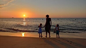Un coucher de soleil sur l’océan, avec une famille se promenant sur la plage.