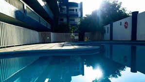 Une piscine dont l’eau est si claire qu’elle reflète parfaitement l’environnement, entourée d’une clôture et de bâtiments.