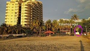 Une plage avec un grand hôtel, des palmiers et une zone délimitée par une clôture.