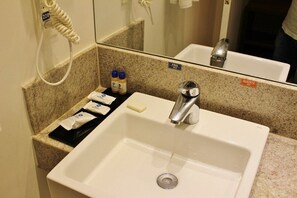 Sink area with a mirror, towel dispenser, and trash bin, featuring a hot water faucet and amenities.