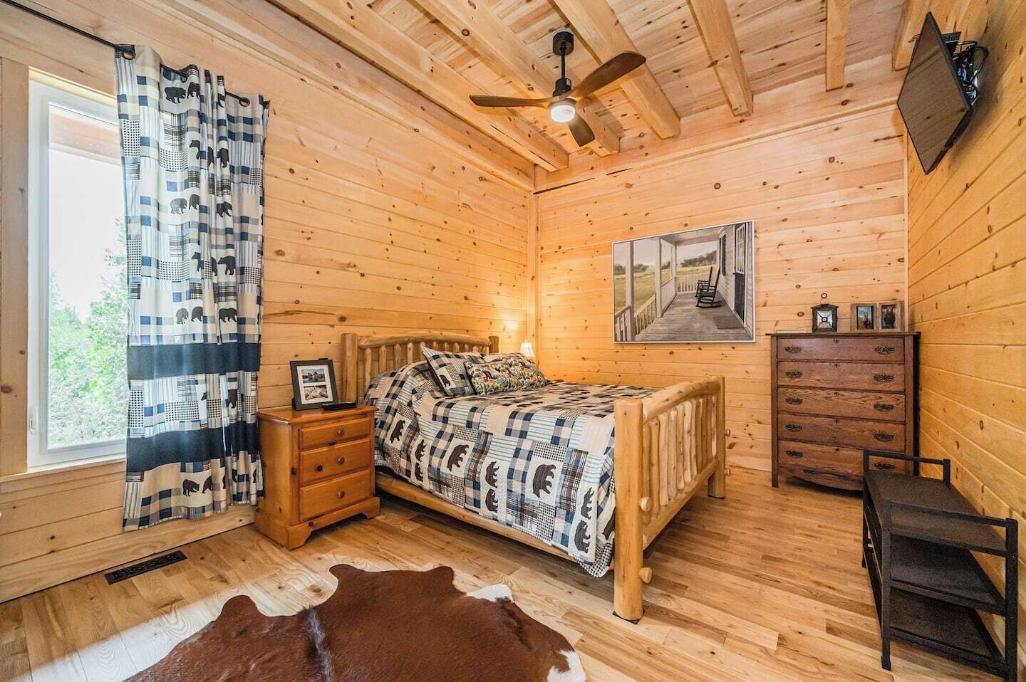 A wooden room with a bed, a nightstand, a dresser, and a ceiling fan.