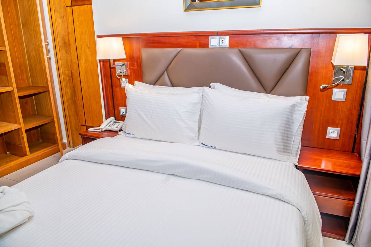 A hotel room with a bed, wooden wardrobe, bedside lamp, and a telephone.