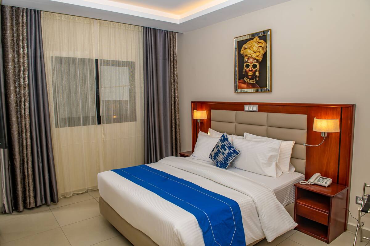 A hotel room with a large bed, two bedside lamps, a nightstand with a phone, and a painting on the wall.