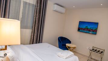 Une chambre d’hôtel avec un lit, une chaise bleue, un téléviseur fixé au mur et un appareil de climatisation.