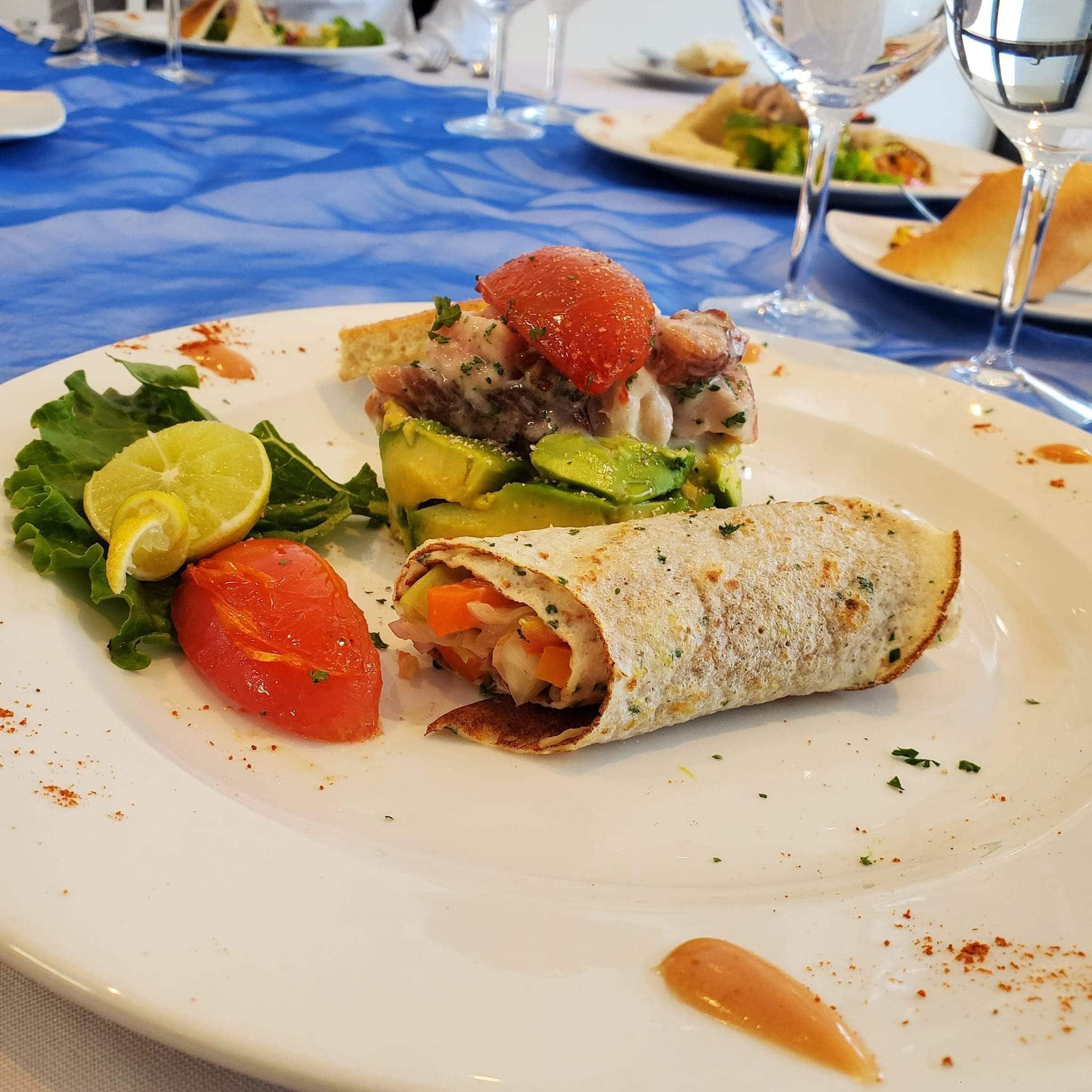 A plate with a wrap, a slice of tomato, and a wedge of lime on a table with a blue tablecloth.
