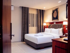Une chambre d’hôtel avec un lit, des lampes de chevet, une table de chevet en bois et une œuvre d’art encadrée au mur.