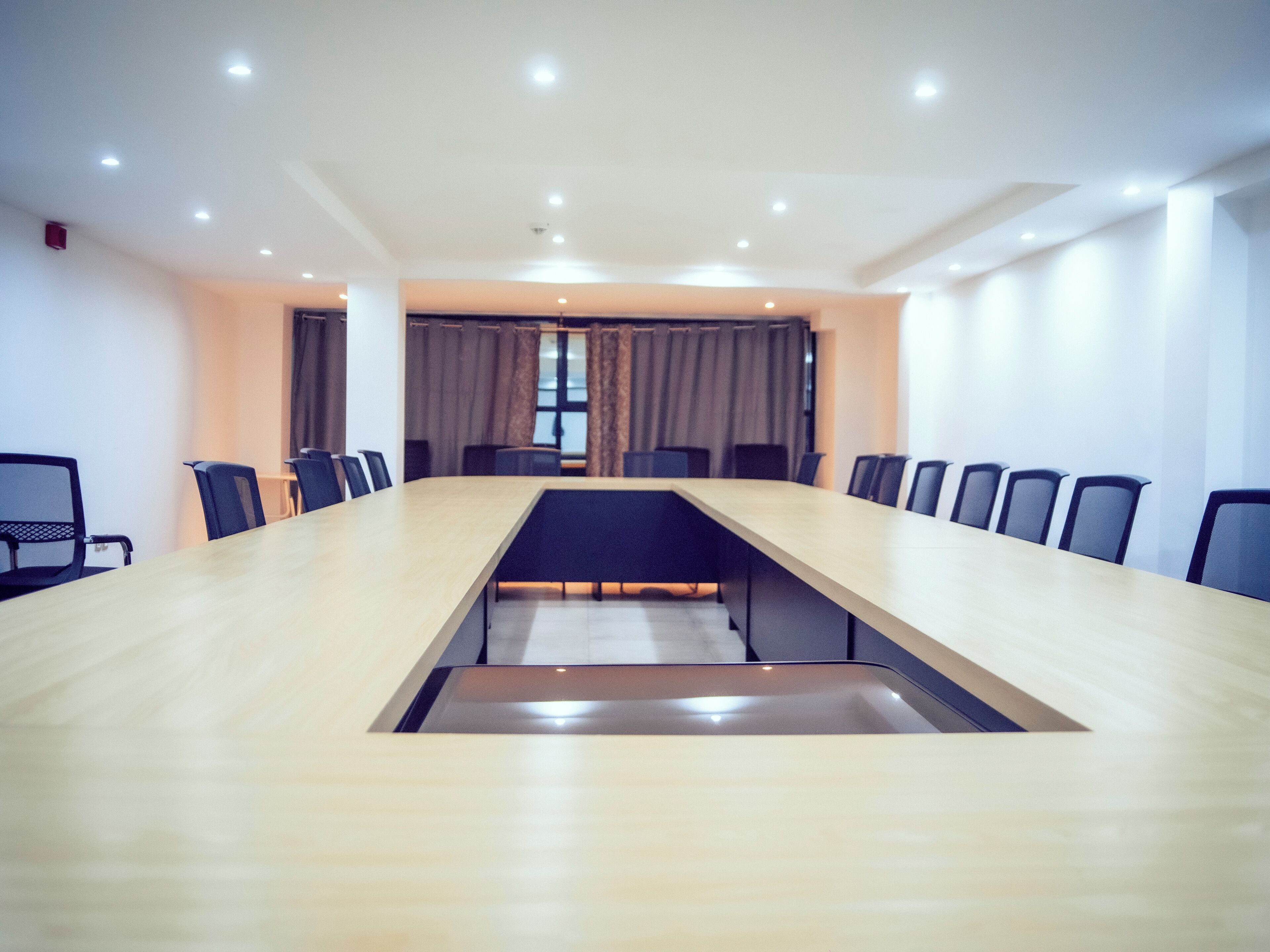Un salón de conferencias con una mesa larga, sillas y un ventanal con cortinas.