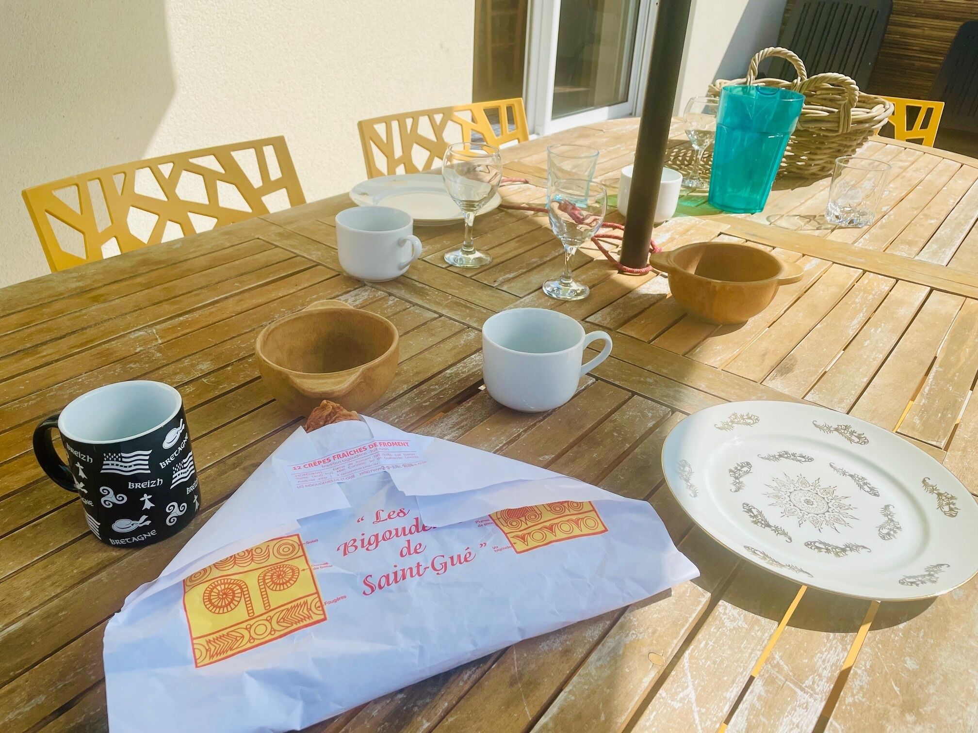 Una mesa de madera con una bolsa de papel blanca que dice 'Les Bigoudes de Saint-Gué' y un plato con un diseño floral.