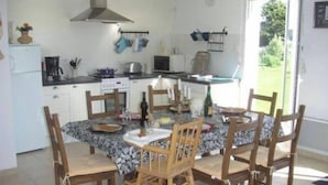A kitchen with white cabinets, a stove, and a dining area with a table and chairs. - Plain pied at eckmuhl lighthouse  (Penmarc'h)