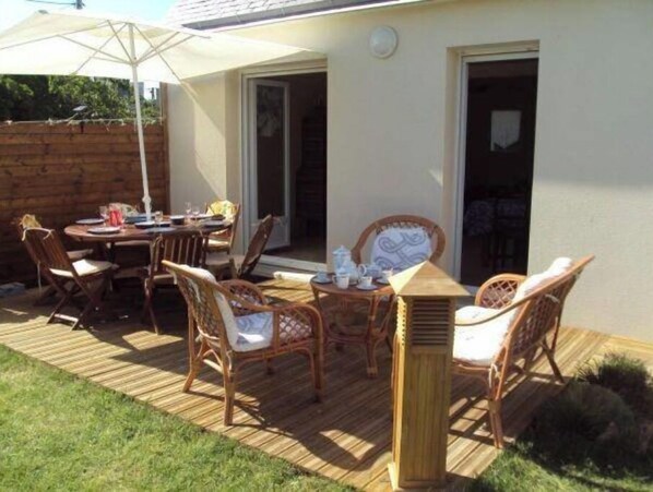 An outdoor patio with a wooden deck, wicker furniture, and a table set for dining.