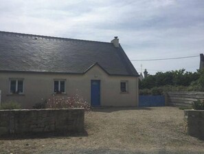 A single-story house with a blue door, a stone wall in front, and a gravel driveway.