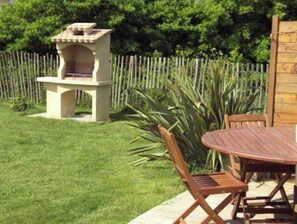A patio with a wooden table and chairs, a stone barbecue grill, and a wooden fence.