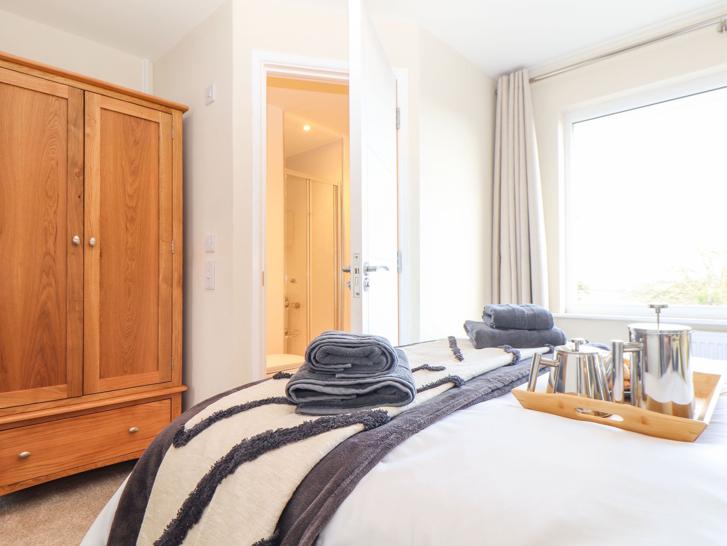A hotel room with a wooden wardrobe, a bed with a striped blanket, a set of towels, and a window with curtains.