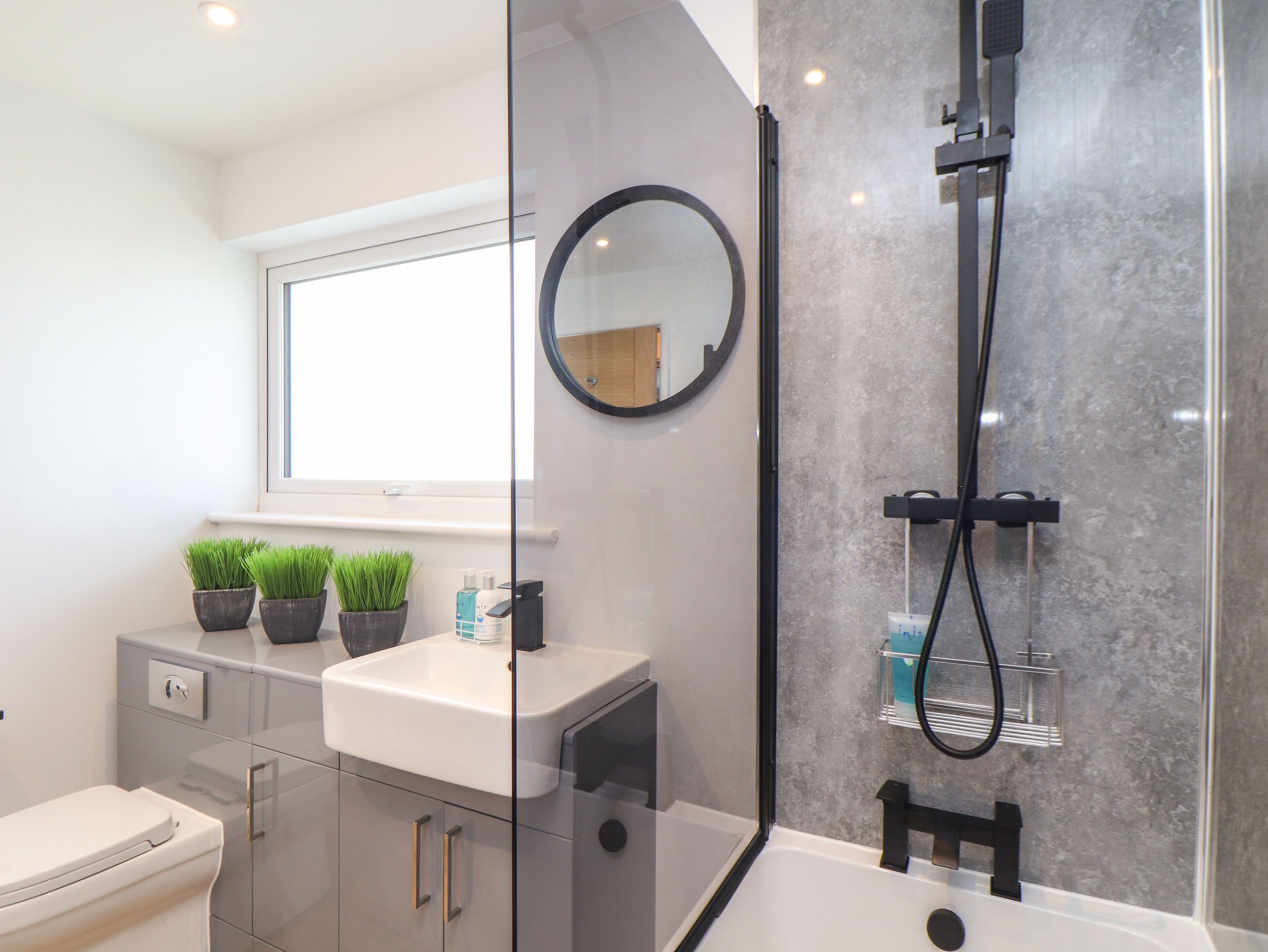 Un baño moderno con separador de vidrio, un lavabo blanco, un espejo y zona de ducha.