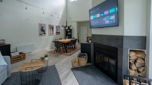Un vaste salon doté d’une cheminée, d’un coin repas et d’un téléviseur fixé au mur, qui permet d’accéder aux services de diffusion en continu.
