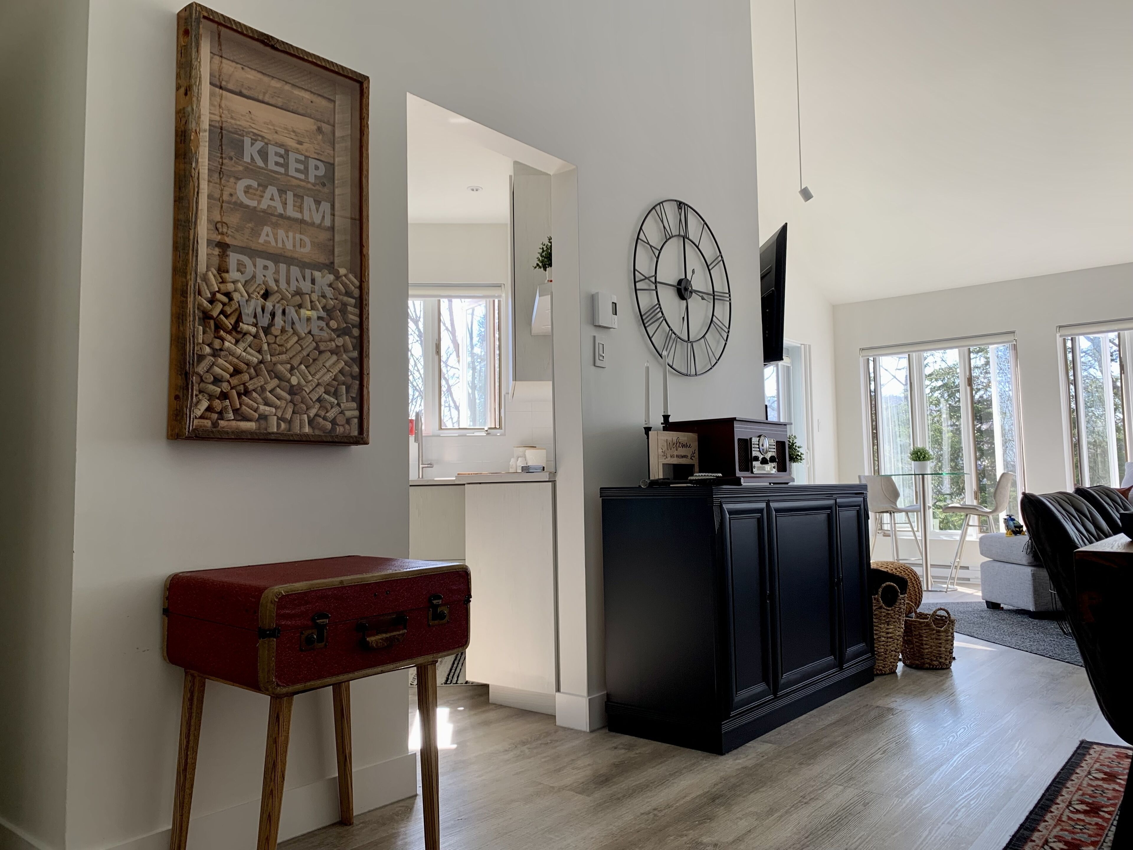 A spacious living area with a wooden floor, a red suitcase, a black entertainment unit, and a clock on the wall.