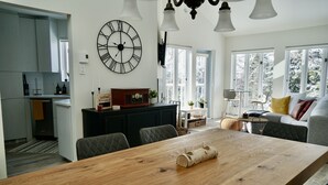 Une cuisine moderne avec une table à manger en bois, une grande horloge murale et un coin salon confortable avec un canapé et des fauteuils.