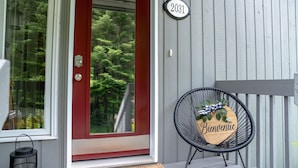 Une porte rouge avec une plaque portant le numéro « 2031 », une chaise noire avec une pancarte « Bienvenue » et un paillasson.