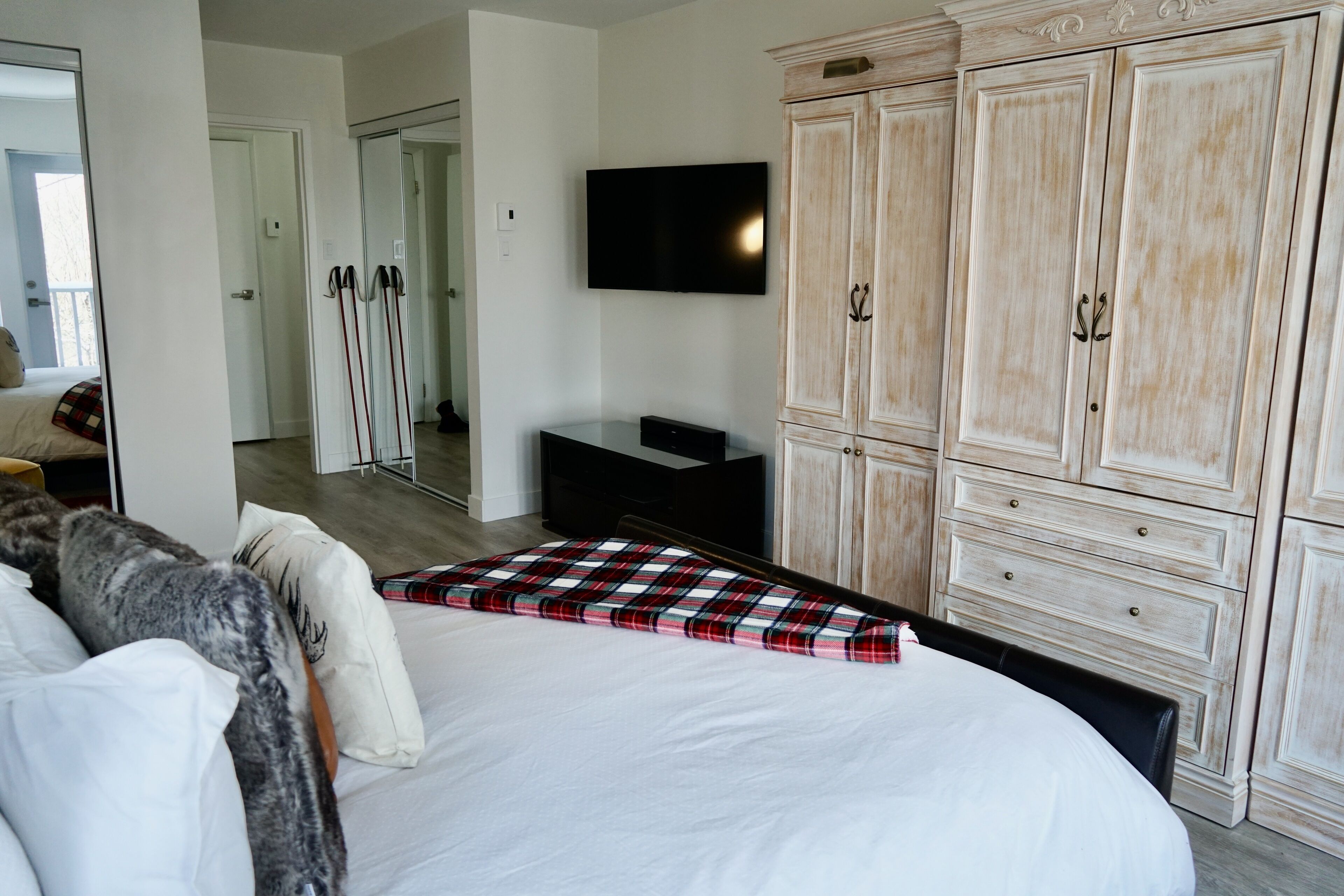 A bedroom with a large bed, a television mounted on the wall, and a wardrobe with multiple drawers.