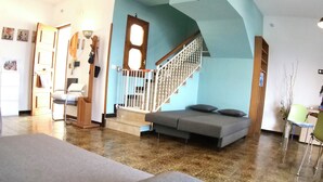 Amplia sala de estar con una escalera que sube a un piso superior, un sofá y un comedor.